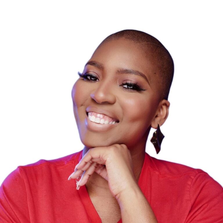 Smiling person with a shaved head wearing a red shirt and dangling earrings, resting their chin on their hand against a white background.